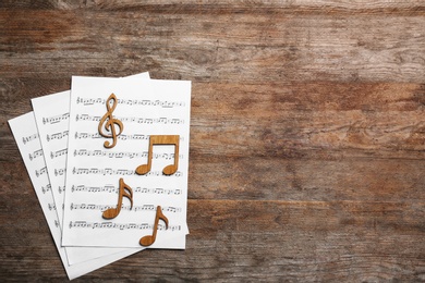 Music notes with sheets on wooden background, flat lay. Space for text