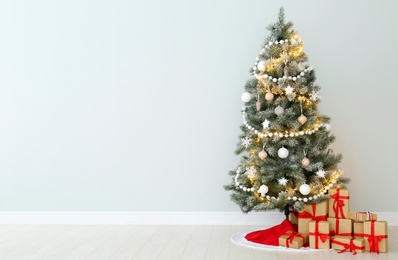 Photo of Decorated Christmas tree with red skirt and gifts indoors, space for text