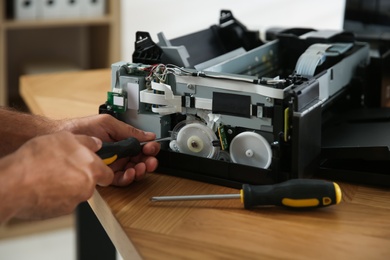 Repairman with screwdriver fixing modern printer indoors, closeup