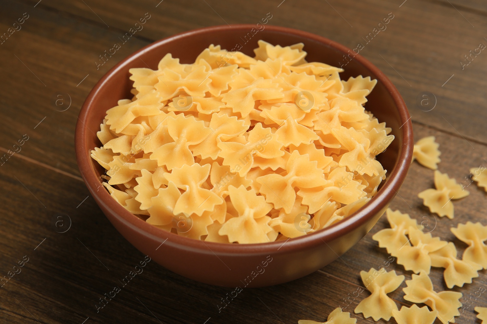 Photo of Raw farfalle pasta in bowl on wooden table, closeup