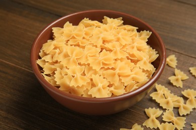 Raw farfalle pasta in bowl on wooden table, closeup