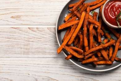 Delicious sweet potato fries served with sauce on white wooden table, top view. Space for text
