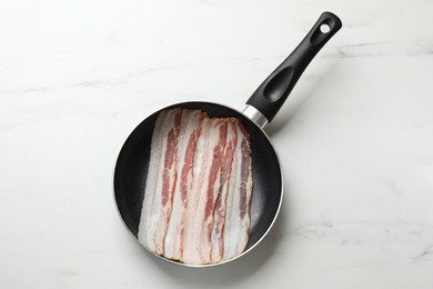 Slices of raw bacon in frying pan on white marble table, top view