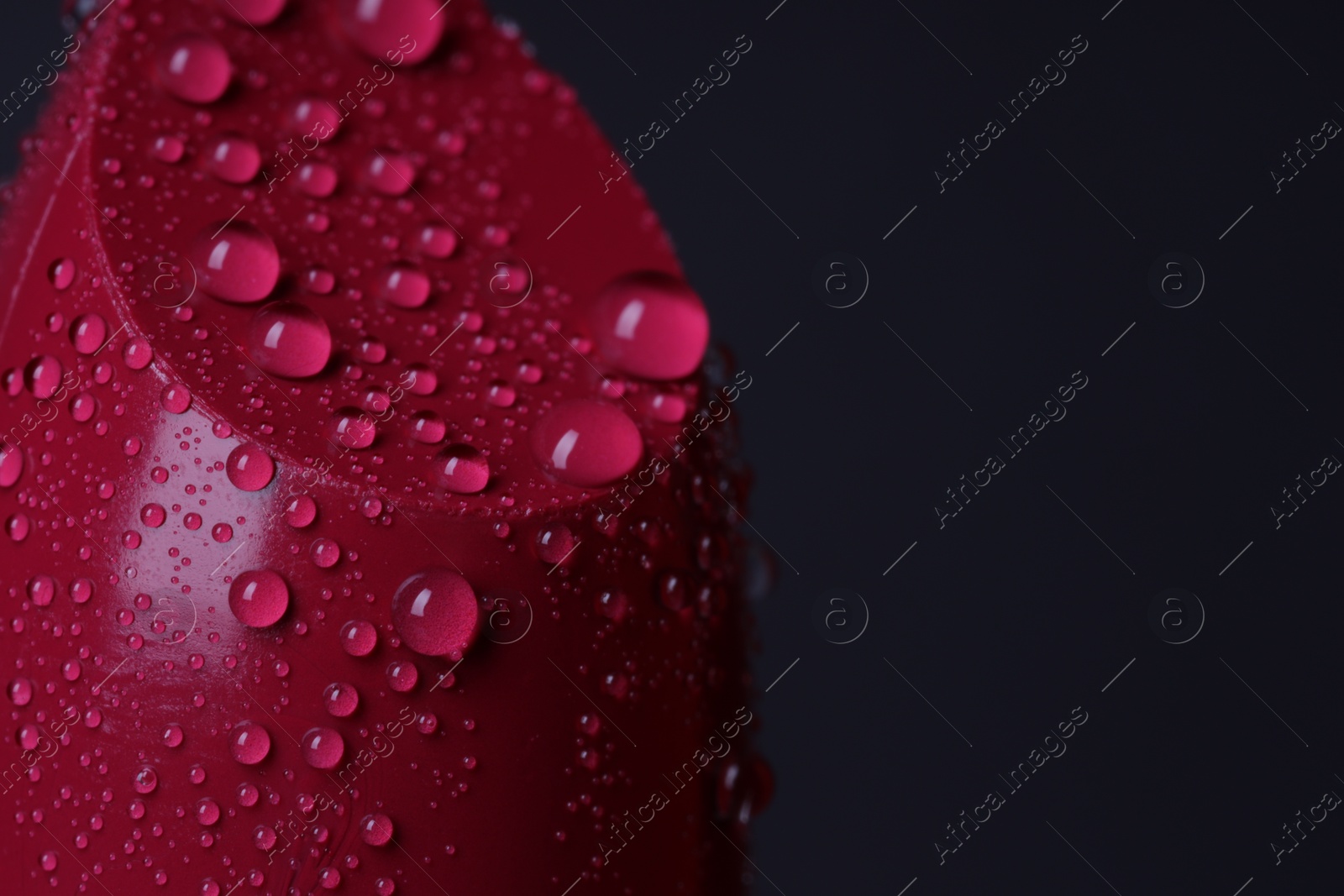 Photo of Red lipstick with water drops on dark gray background, macro view. Space for text