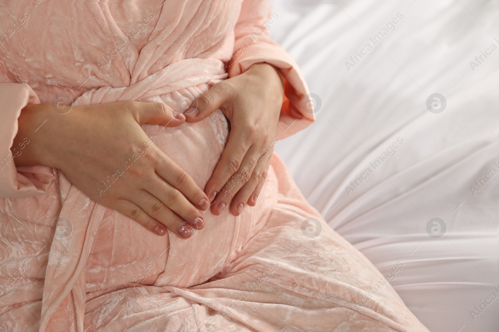 Photo of Pregnant woman in bathrobe on bed, closeup