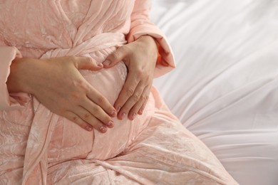 Photo of Pregnant woman in bathrobe on bed, closeup