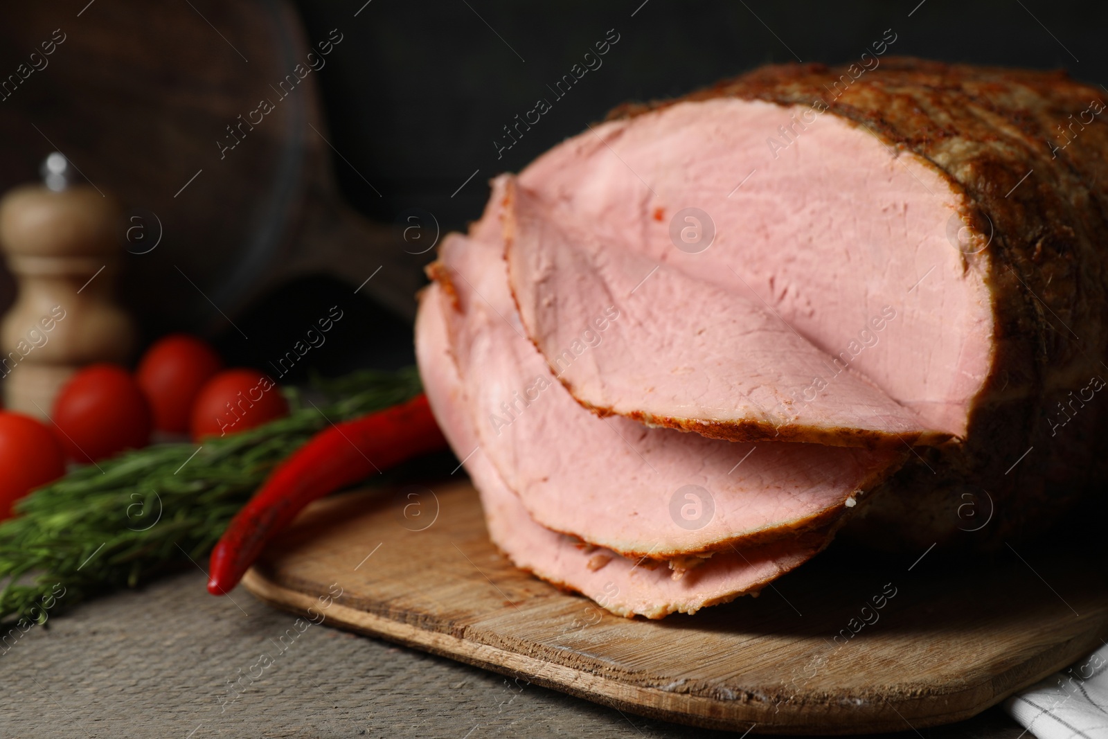 Photo of Delicious baked ham, tomatoes, chili pepper and rosemary on grey wooden table, closeup