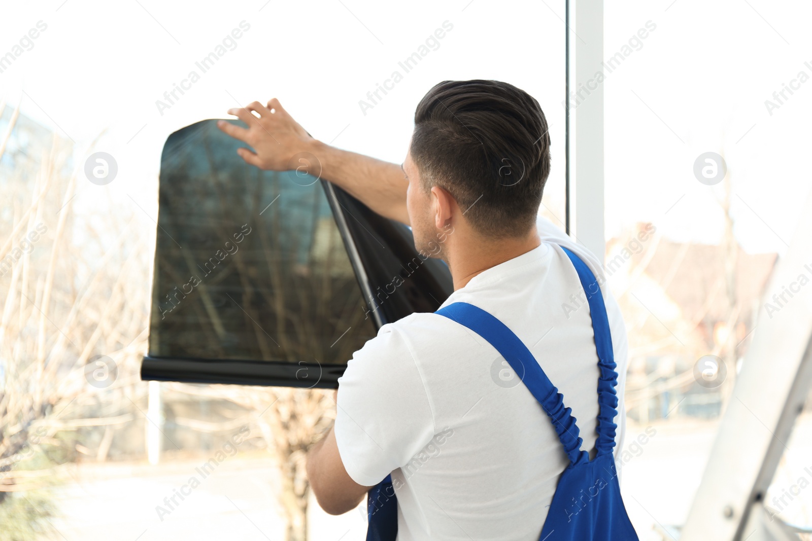 Photo of Professional worker tinting window with foil indoors