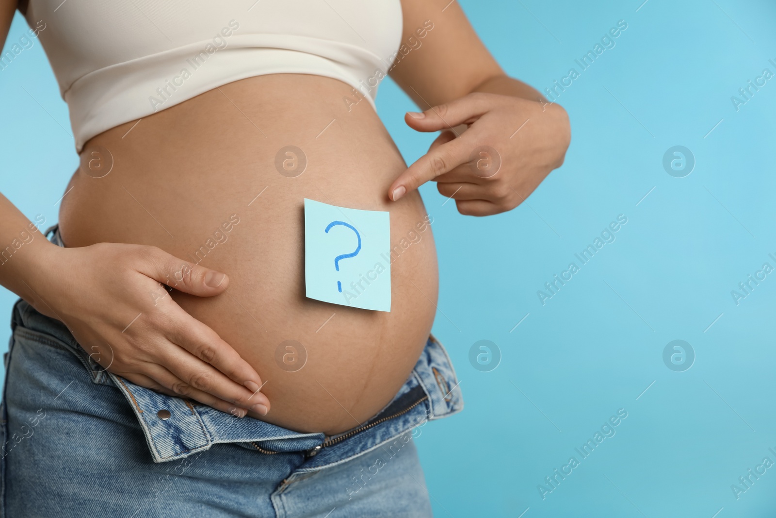 Photo of Pregnant woman with sticky note on belly against light blue background, closeup. Choosing baby name