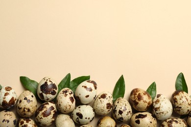 Speckled quail eggs and green leaves on beige background, flat lay. Space for text