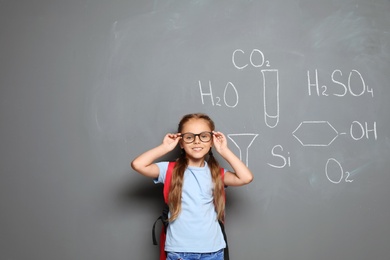 Photo of Little school child with backpack and chemical formulas on grey background