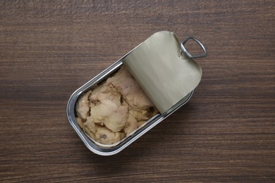 Photo of Open tin can of tasty cod liver on wooden table, top view