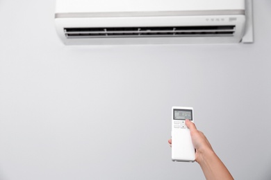 Photo of Woman operating air conditioner with remote control indoors, focus on hand