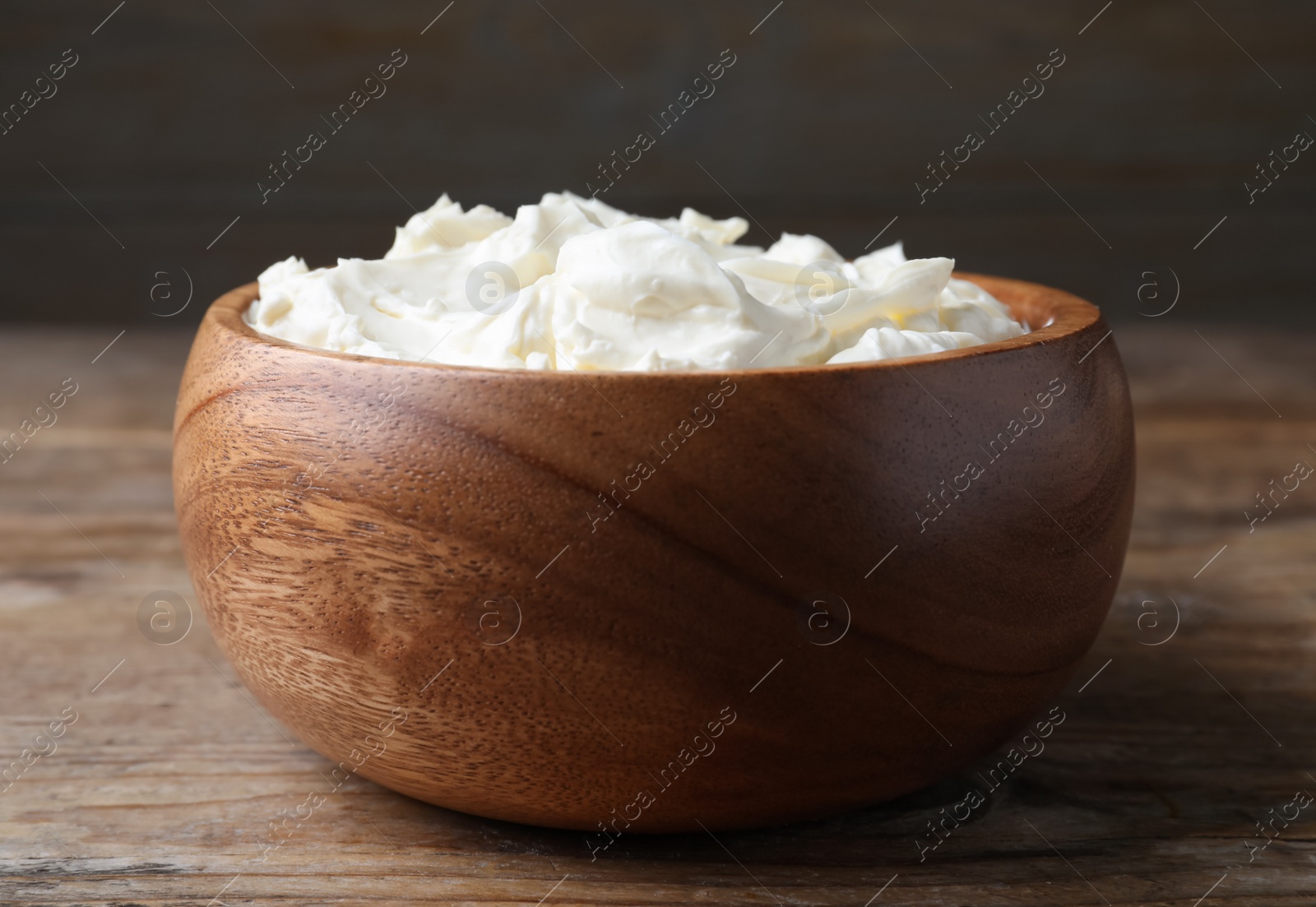 Photo of Bowl of tasty cream cheese on wooden table, closeup