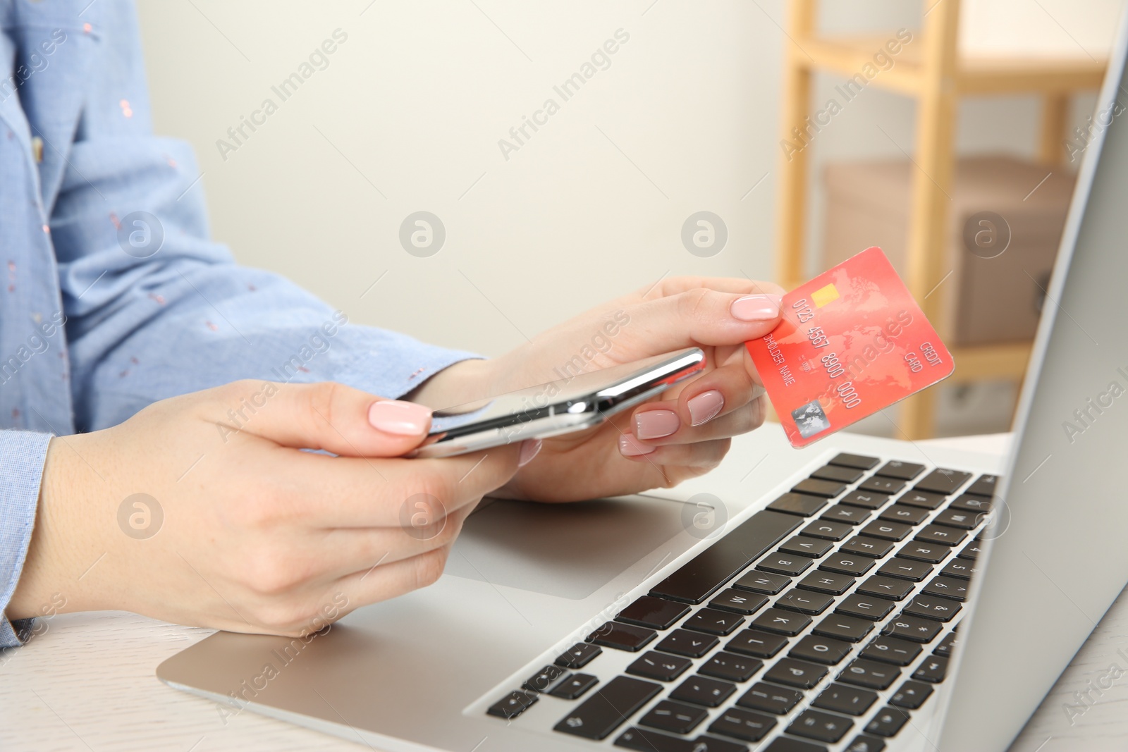 Photo of Online payment. Woman using credit card and smartphone near laptop at white wooden table indoors, closeup