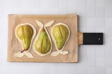 Board with raw dough and fresh pears on white tiled table, top view
