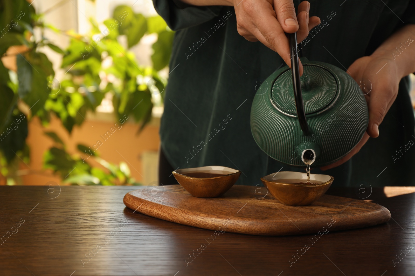 Photo of Woman pouring freshly brewed tea from teapot into cup at wooden table indoors, closeup and space for text. Traditional ceremony