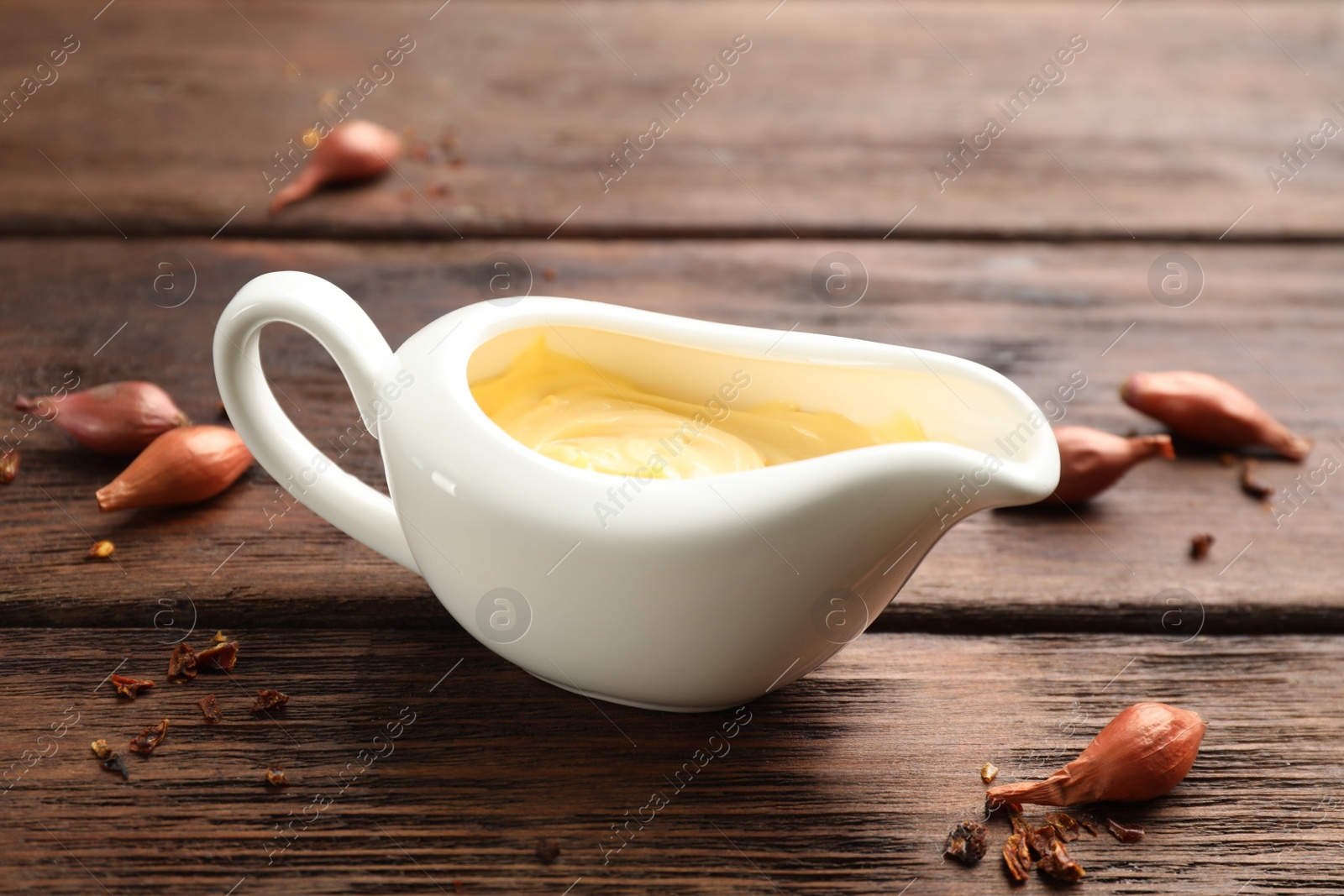 Photo of Tasty sauce in gravy boat, small onion bulbs and spice on wooden table