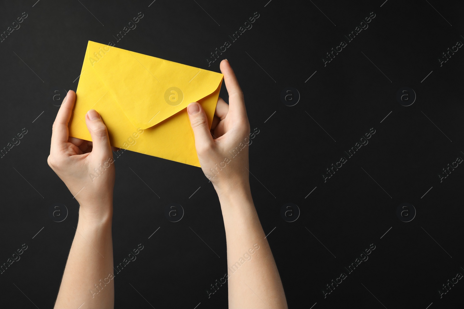 Photo of Woman holding yellow paper envelope on black background, closeup