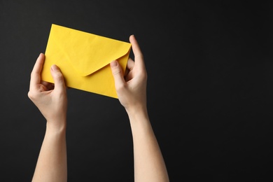 Woman holding yellow paper envelope on black background, closeup