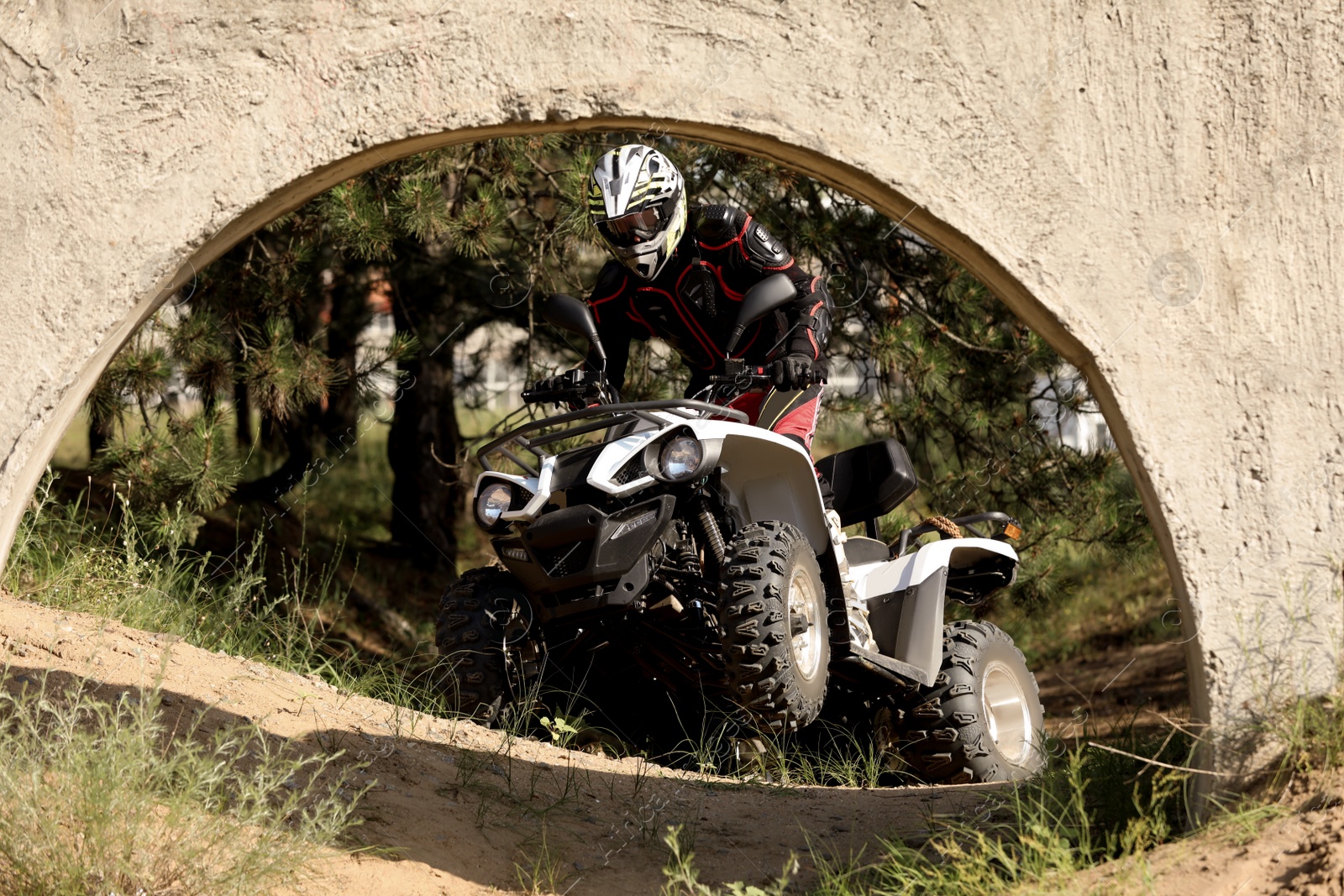 Photo of Man driving modern quad bike on sandy road near forest. Extreme sport