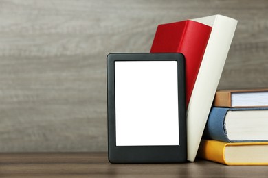 Photo of Portable e-book reader and many hardcover books on wooden table, space for text