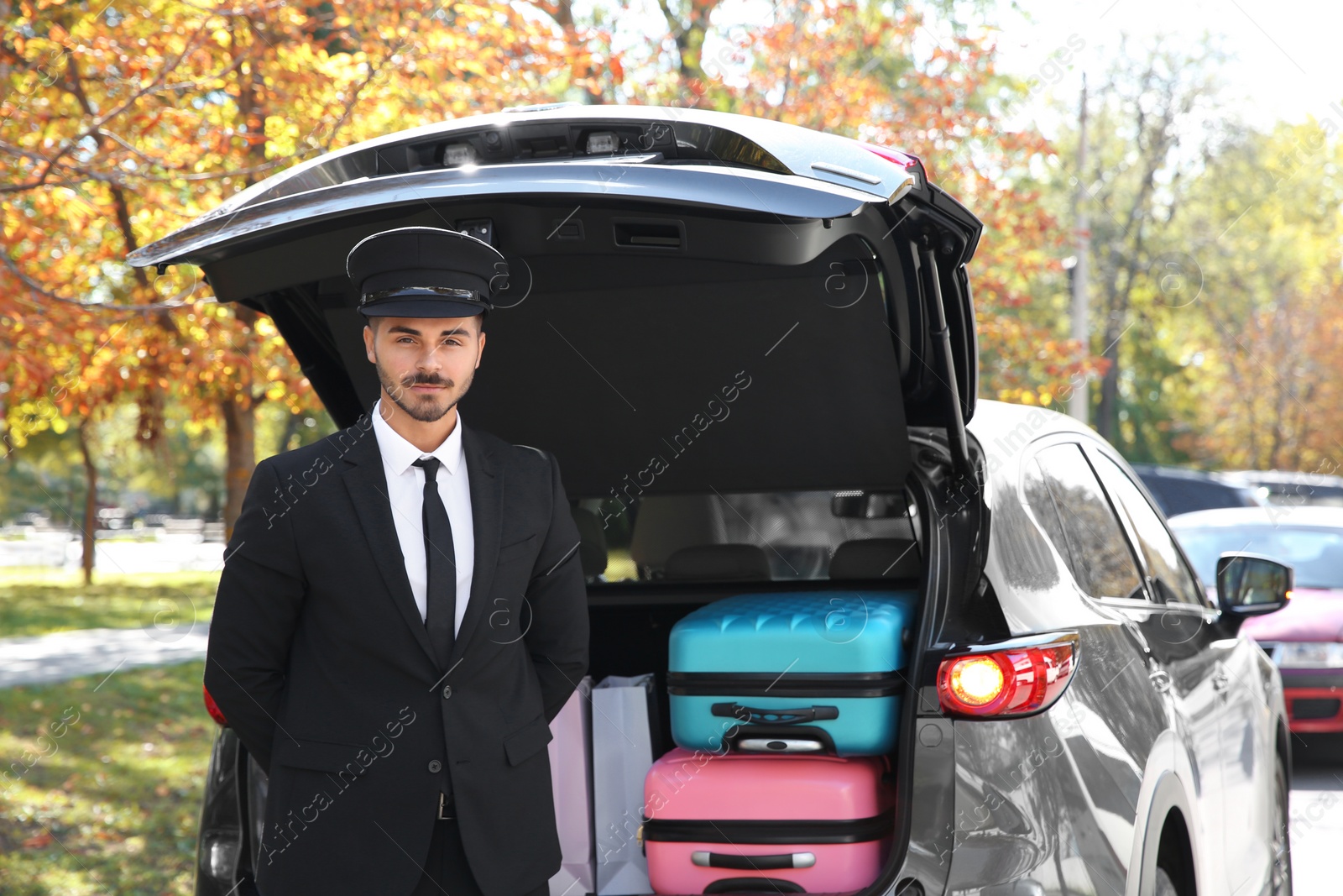 Photo of Young driver standing near car with open trunk outdoors