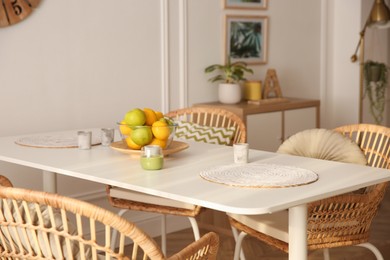 Stylish white dining table and wicker chairs in room. Interior design