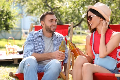 Smiling friends clinking bottles on picnic in park on summer day