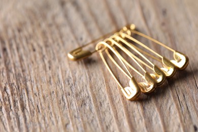 Golden safety pins on wooden table, closeup. Space for text