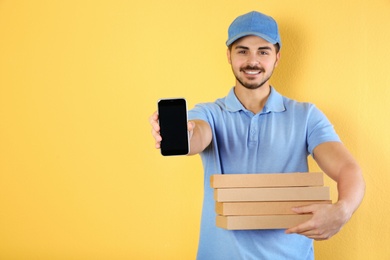 Photo of Young man holding pizza boxes and smartphone on on color background, mockup for design. Online food delivery