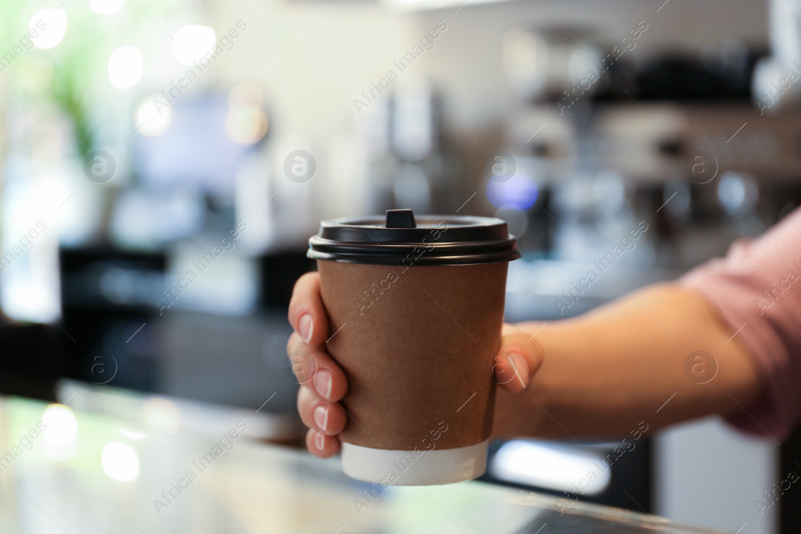Photo of Barista putting takeaway paper cup with coffee on countertop in cafe, closeup