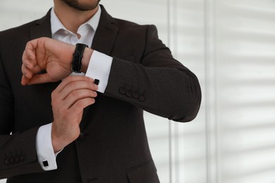 Man wearing stylish suit and cufflinks near white wall, closeup