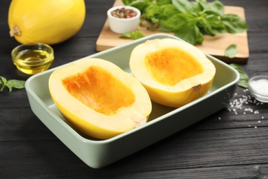 Photo of Raw spaghetti squash halves in baking dish and spices  on dark wooden table