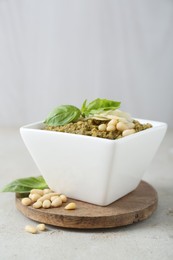 Photo of Bowl with delicious pesto sauce, cheese, pine nuts and basil leaves on light table, closeup