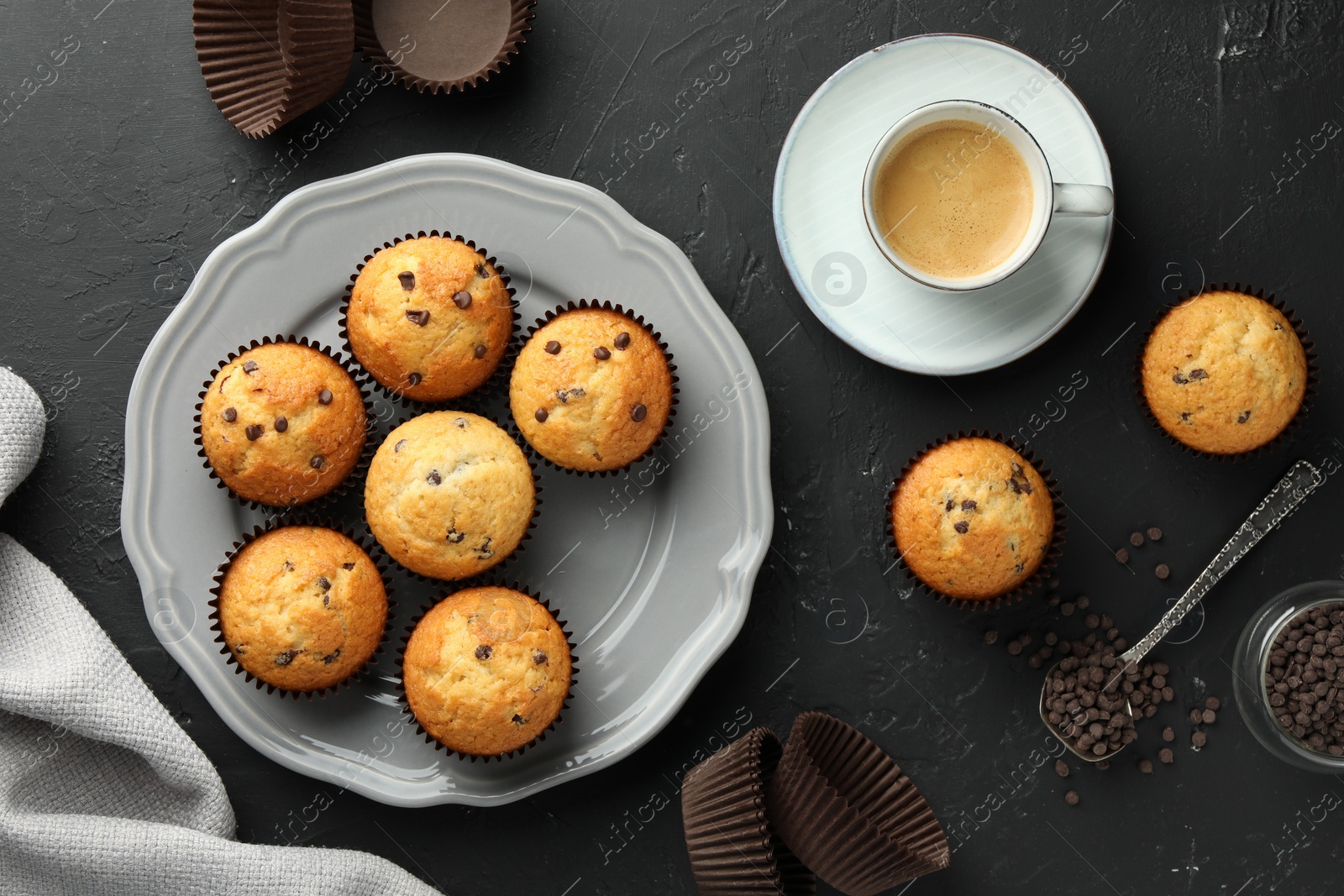 Photo of Delicious freshly baked muffins with chocolate chips and cup of coffee on dark gray table, flat lay