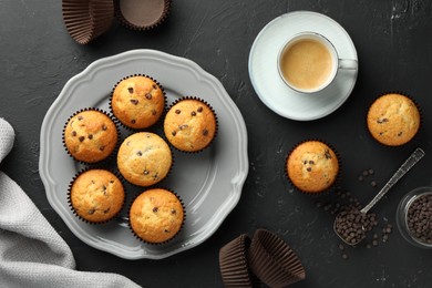 Delicious freshly baked muffins with chocolate chips and cup of coffee on dark gray table, flat lay