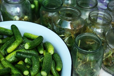 Photo of Glass jars with different herbs and fresh cucumbers on table. Pickling vegetables