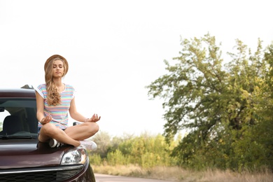 Photo of Young woman meditating on car hood outdoors. Joy in moment
