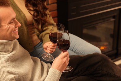 Happy lovely couple with glasses of wine resting together near fireplace at home, closeup