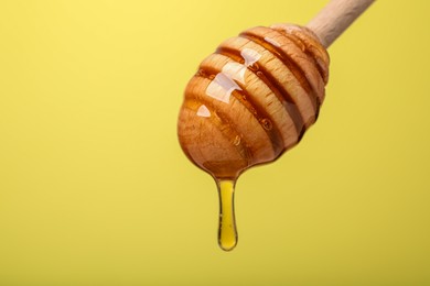 Delicious honey flowing down from dipper against yellow background, closeup. Space for text