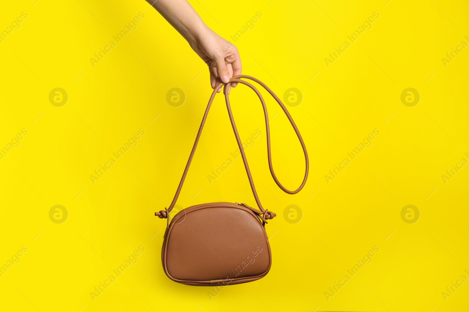 Photo of Woman holding stylish bag on yellow background, closeup