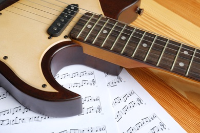 Modern electric guitar and music sheets on wooden background