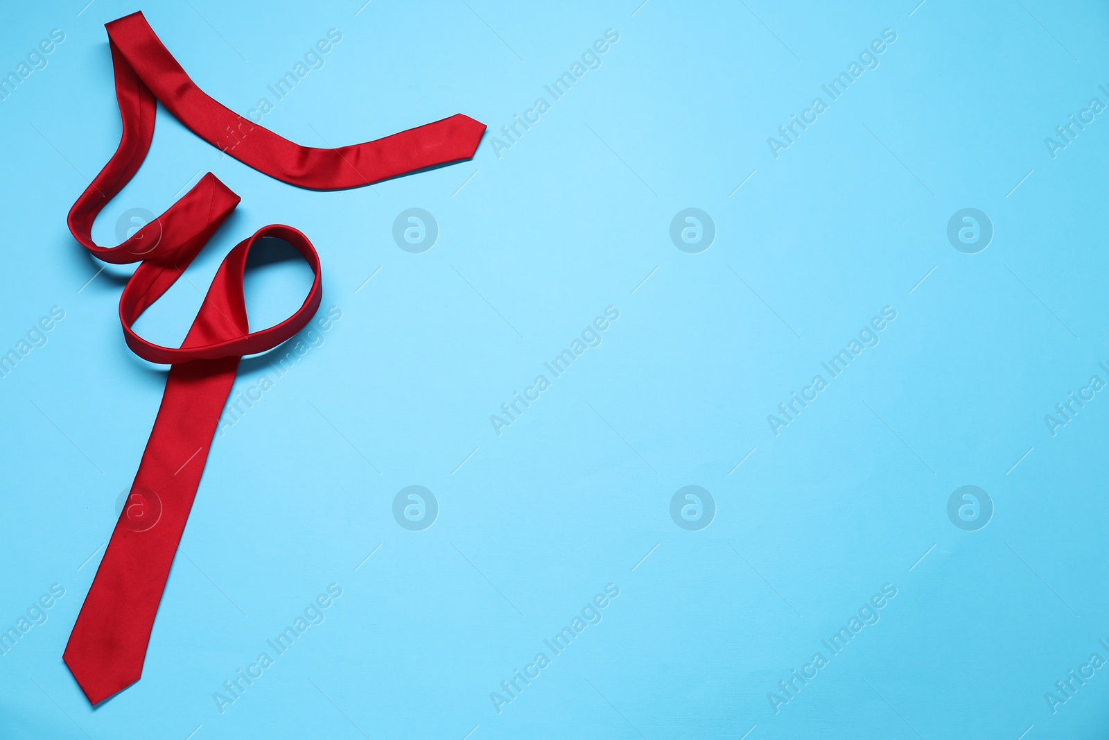 Photo of Red necktie on light blue background, top view. Space for text