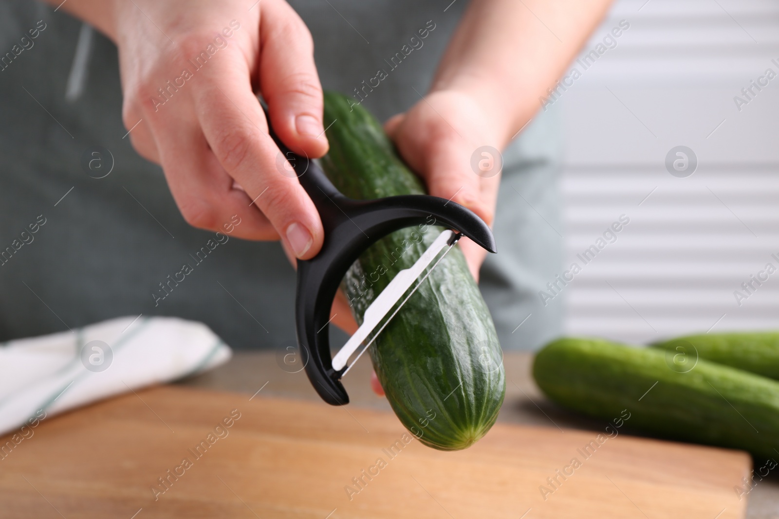 Photo of Woman peeling cucumber at wooden table indoors, closeup