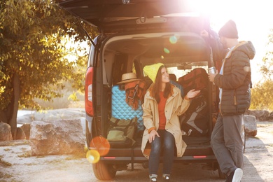 Photo of Young couple packing camping equipment into car trunk outdoors. Space for text