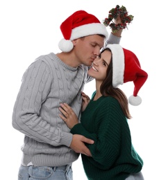 Photo of Happy man kissing his girlfriend under mistletoe wreath on white background