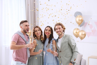 Happy friends with champagne in glasses and confetti at home