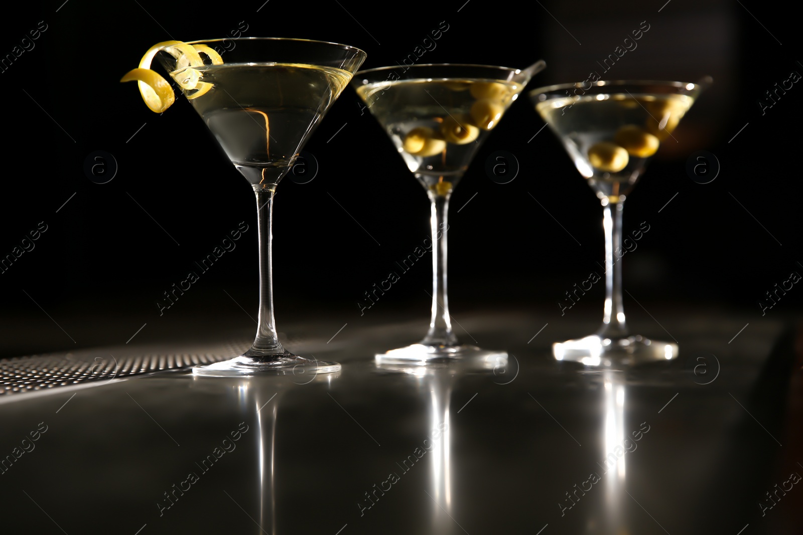 Photo of Glasses of martini cocktail with olives and lemon peel on bar counter. Space for text