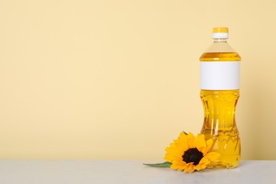 Photo of Bottle of cooking oil and sunflower on white table, space for text